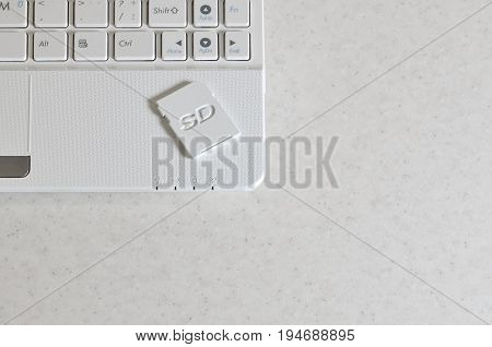 A Compact Sd Memory Card Lies On A White Netbook. The Digital Information Storage Device Is Ready Fo