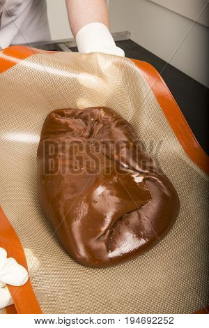 Artisanal production of caramel toffee sweets butterscotch candies. Woman with white lab coat blouse stretching moving extending the sugar pastry to do butterscotch candies sweet of France