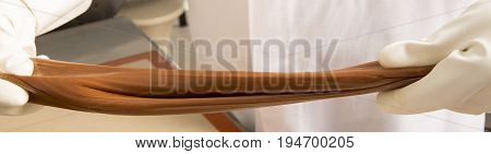 Artisanal production of caramel toffee sweets butterscotch candies. Woman with white lab coat blouse stretching moving extending the sugar pastry to do butterscotch candies sweet of France