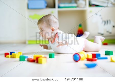 Cute happy smiling baby playing with colorful wooden blocks toys. New born child, little girl looking at the camera and crawling. Family, new life, childhood, beginning concept. Baby learning grab