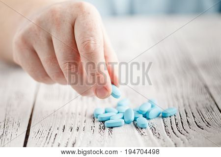 Male Hand Holding Blue Pill Between Fingers
