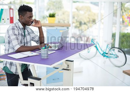 Smiling executive talking on mobile pone while using laptop in office