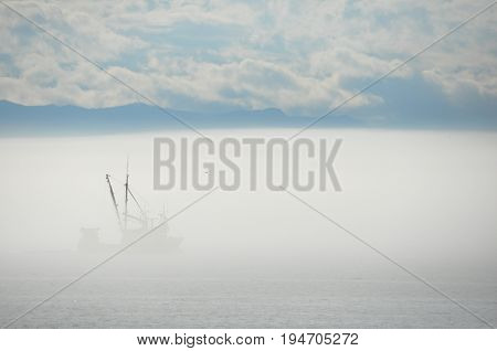A lonely fishing trawler navigates through the fog bank on its way home with its bounty.