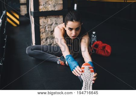 Beautiful slim and sporty girl doing stretching exercises sitting on th floor in th gym. Serious girl is warming up before the training or boxing. Close up