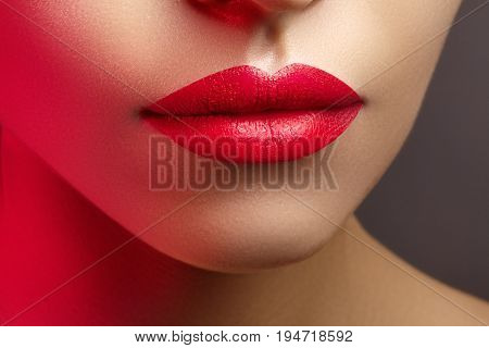 Cosmetics makeup and trends. Bright lip gloss and lipstick on lips. Closeup of beautiful female mouth with red lip makeup. Beautiful part of female face. Perfect clean skin in red light