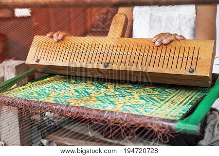 old asian woman working behind thai domestic tool for making natural reed mat for home living