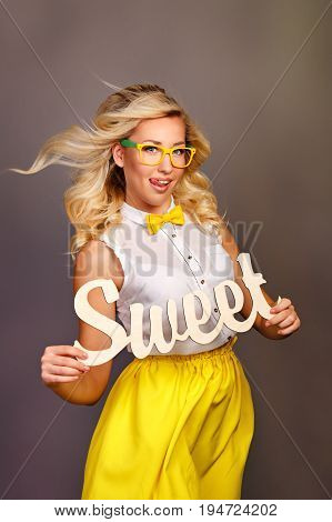 Young attractive girl holding an inscription of a sweet girl. She is wearing a blouse a bow tie and glasses.