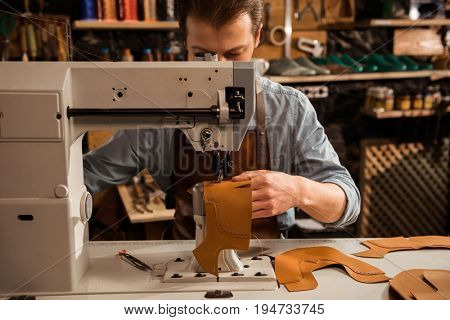 Man cobbler stitching leather patrs on a sewing machine