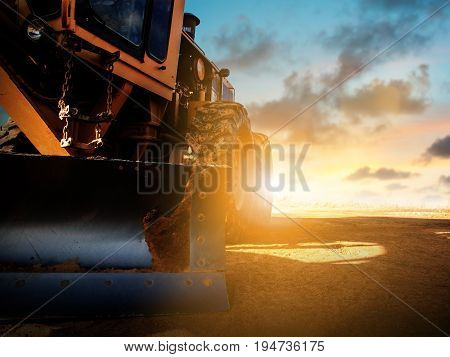 Silhouette Wheel loader Excavator with backhoe unloading sand at eathmoving works in construction site over blurred natural background sunset pastel. heavy industry and safety at work concept.