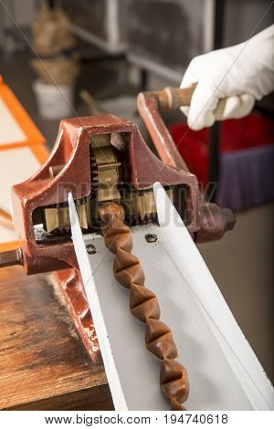 Artisanal production of caramel toffee sweets butterscotch candies. Woman with white lab coat blouse cutting rolls of sugar pastry to do butterscotch candies traditional sweetx of France