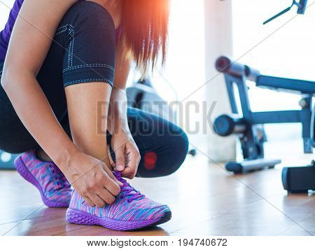 Running shoes - closeup of woman tying shoe laces. Female sport fitness runner getting ready for jogging in gym room with fitness equipments in backgroound