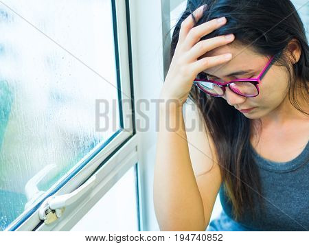 Woman Depressed or sad woman wear glasses sitting alone and covering her face due to having a head ache near the window.