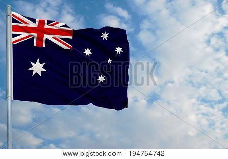 National flag of Australia on a flagpole in front of blue sky.