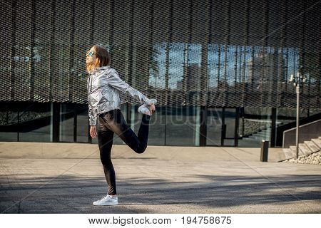 Lifestyle portrait of a stylish woman in silver jacket exersicing outdoors in the modern urban environment
