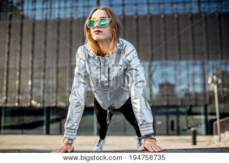 Lifestyle portrait of a stylish woman in silver jacket exersicing outdoors in the modern urban environment