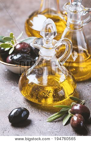 Olive oil in a glass bottle and olive branch on brown stone table