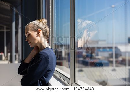 Tired businesswoman looking lown while standing by window in office