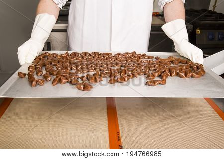 Artisanal production of caramel toffee sweets butterscotch candies. Woman with white lab coat blouse shaking separating removing the pieces of butterscotch candies traditional sweets of France