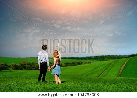 Young Couple Standing On Green Field, Woman Showing Her Hand At The Stars