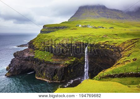 Dramatic waterfall on Faroe Islands and the village Gasadalur in the background. Rainy day in july.