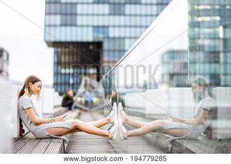 Lifestyle portrait of a business woman dressed casually sitting with phone outdoors at the modern district in Dusseldorf city, Germany