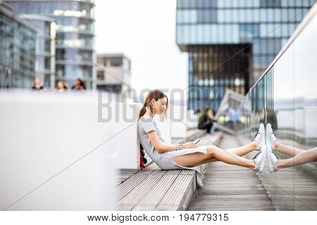 Lifestyle portrait of a business woman dressed casually sitting with phone outdoors at the modern district in Dusseldorf city, Germany