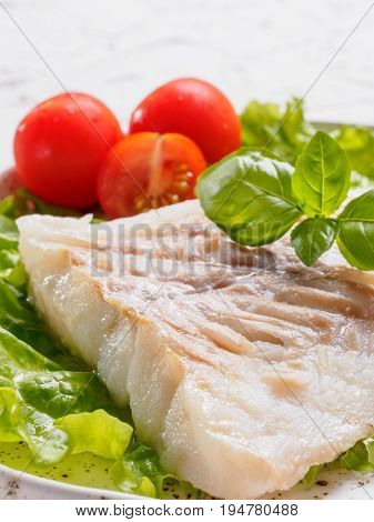 Close up view of grilled codfish with basil and cherry tomatoes in trendy white plate.
