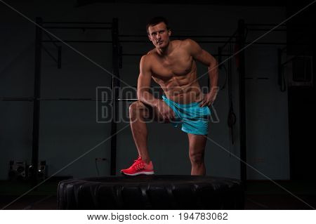 Portrait of confident young man with naked torso exersicing with hummer and tire. Weightlifting or functional training. Sports and fitness concept.