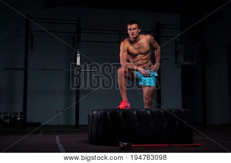 Portrait of confident young man with naked torso exersicing with hummer and tire. Weightlifting or functional training. Sports and fitness concept.