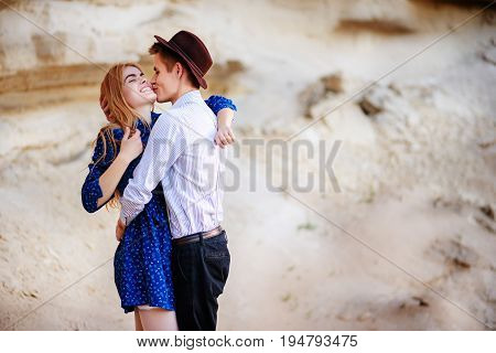 An Attractive Man Is Hugging And Kissing An Beautiful Woman In A Blue Dress In The Middle Of A Sandy