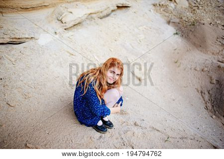 Woman With Long Carrot Hair Is Crouching And Hugging Herself In The Middle Of A Sandy Canyon