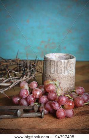 Communion table with wine cup, grapes, nails and crown of thorns over blue background