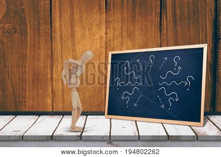 Wooden 3d figurine standing with hands on back against black board on a wooden table