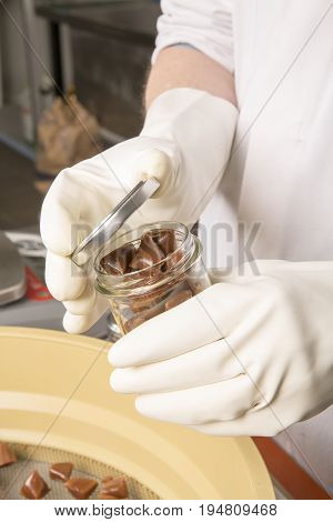 Artisanal production of caramel toffee sweets butterscotch candies. Woman with white gloves shaking put in jar get in the jugs the pieces of butterscotch candies traditional sweets of France