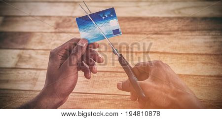 Cropped hands of businessman cutting credit card with scissors on table