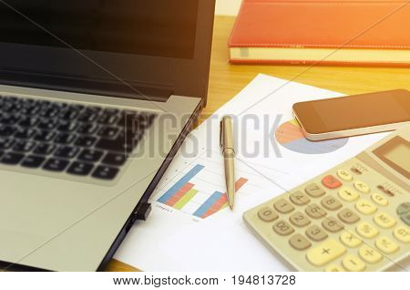 close up business accessories laptop calculator datasheet pen notebook and smartphone on desk financial report saving and economy business concept sunlight effect soft focus selective focus