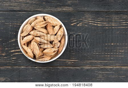 Ceramic bowl filled with Uzbek inshell almonds on wooden background