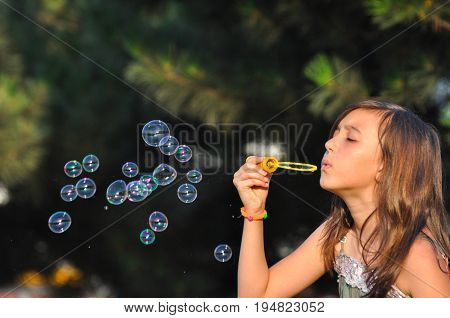 Adorable girl blowing soap bubbles in summer park. Girl play in park and blowing soap bubbles