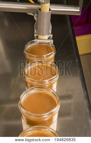 Automated food factory machine get the caramel jam in the jugs. Close up