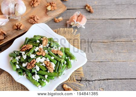 Green string beans with cottage cheese and walnuts on a white plate and vintage wood background with copy space for text