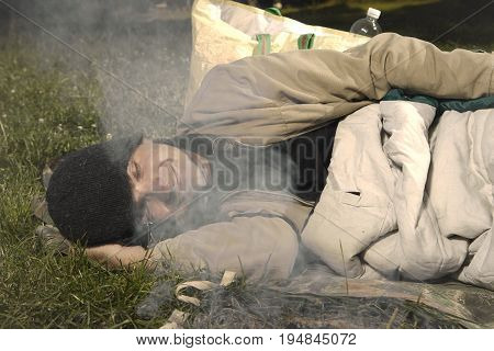 Vagabond young man sleeping in park near illegal fireplace