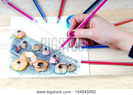 A hand is holding a pencil. Pencil sharpener shavings on the white paper. Back to school