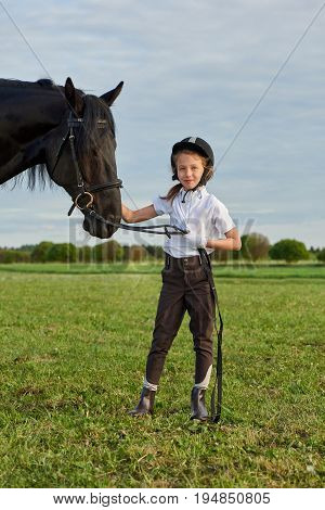 Pretty little girl jockey communicating with her black horse in professional outfit