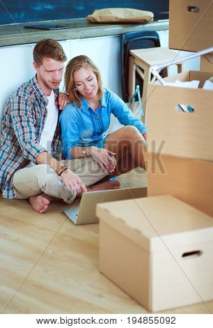 Young couple moving in new home.Sitting on floor and relaxing after unpacking.Looking something on laptop
