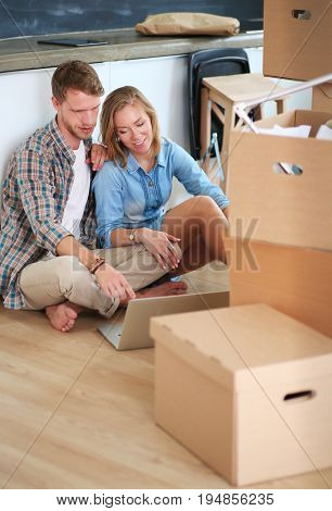 Young couple moving in new home.Sitting on floor and relaxing after unpacking.Looking something on laptop