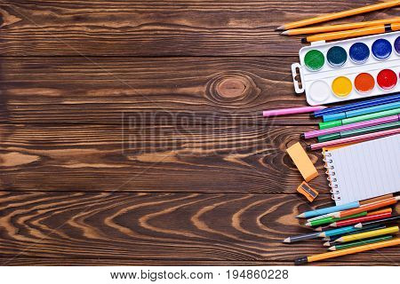 Border from stationery - pencils pen note erazer paint on wooden background. Back to school. Top view. Place for text.