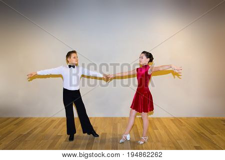 The young boy and girl posing at dance studio on gray. The ballroom dancing concept