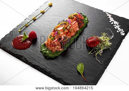 fresh salmon tartar with salt and herbs, studio shot. Fish tartar on black shale