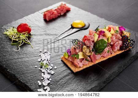 fresh tuna tartar with salt and herbs, studio shot. Fish tartar on black shale