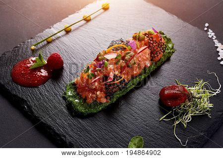 fresh salmon tartar with salt and herbs, studio shot. Fish tartar on black shale
